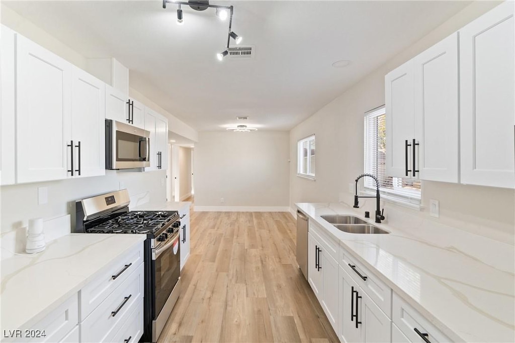 kitchen with white cabinets, sink, appliances with stainless steel finishes, light hardwood / wood-style floors, and light stone counters