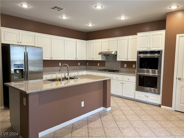 kitchen with light tile patterned flooring, stainless steel appliances, sink, white cabinets, and an island with sink