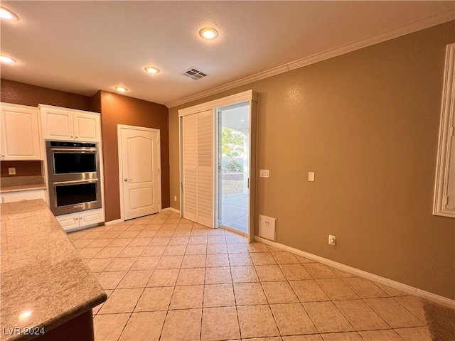 kitchen with double oven, white cabinets, light tile patterned floors, and ornamental molding