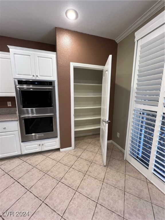 kitchen featuring white cabinetry, stainless steel double oven, crown molding, and light tile patterned floors