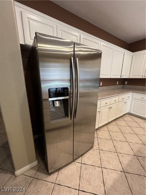 kitchen featuring stainless steel fridge, light tile patterned floors, and white cabinetry