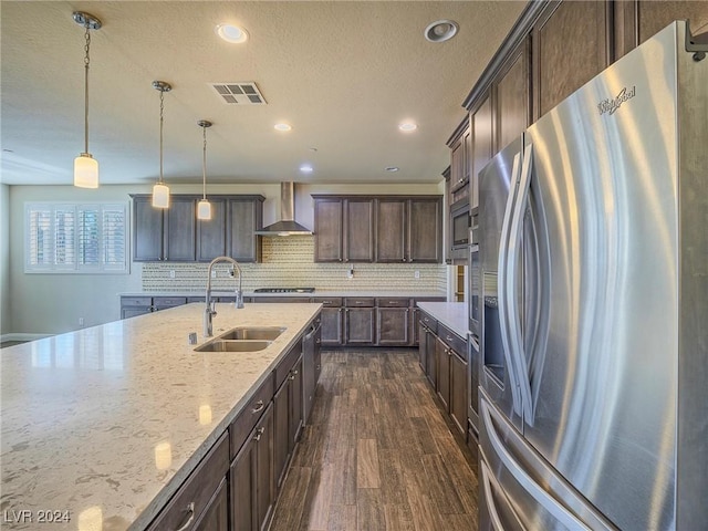 kitchen with appliances with stainless steel finishes, sink, dark brown cabinets, wall chimney range hood, and decorative light fixtures