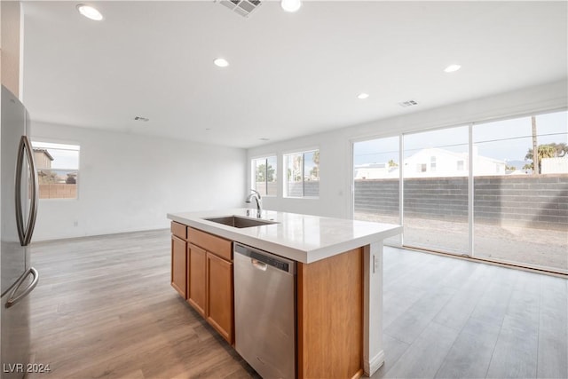 kitchen with sink, a kitchen island with sink, appliances with stainless steel finishes, and light hardwood / wood-style flooring