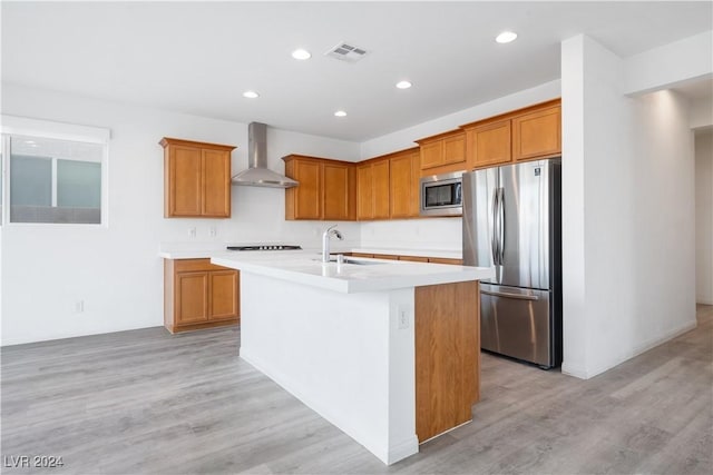 kitchen featuring a center island with sink, sink, light hardwood / wood-style flooring, wall chimney exhaust hood, and appliances with stainless steel finishes