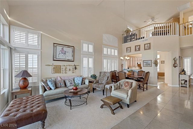 living room with a high ceiling, light tile patterned flooring, and ceiling fan with notable chandelier