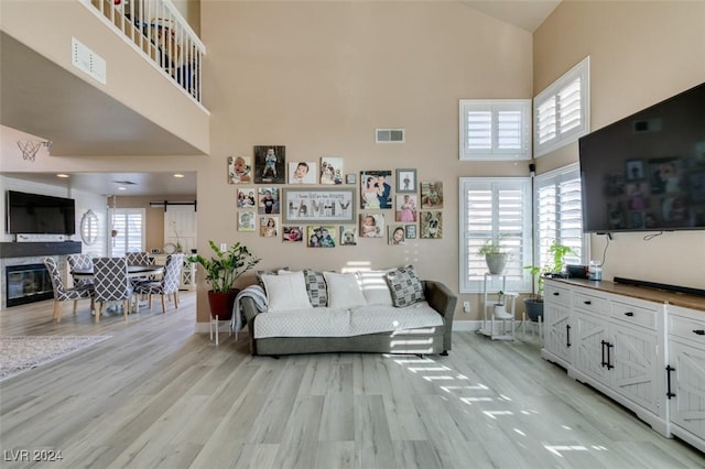 living room with a high ceiling, light hardwood / wood-style floors, a barn door, and a stone fireplace