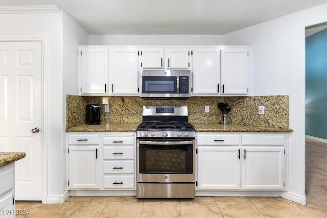 kitchen featuring appliances with stainless steel finishes, backsplash, light tile patterned floors, dark stone countertops, and white cabinets