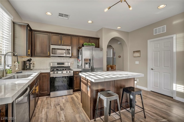 kitchen featuring sink, stainless steel appliances, tasteful backsplash, light hardwood / wood-style floors, and a kitchen island