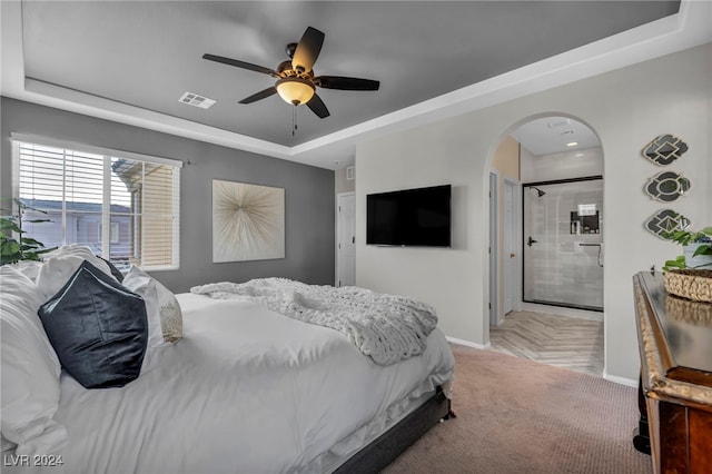 bedroom featuring ensuite bathroom, a raised ceiling, and ceiling fan