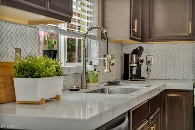 kitchen featuring dark brown cabinets, sink, light stone counters, and backsplash