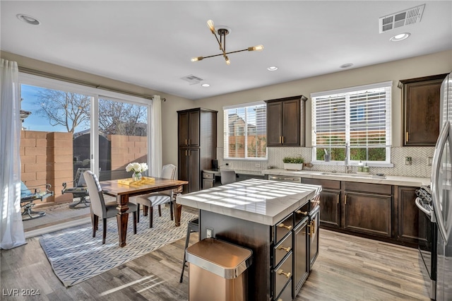 kitchen featuring a center island, light hardwood / wood-style flooring, a notable chandelier, backsplash, and dark brown cabinets