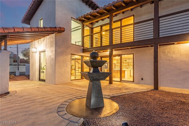 back house at dusk featuring a pergola, a balcony, and a patio