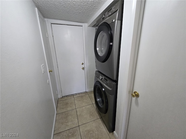 clothes washing area with stacked washer and dryer, light tile patterned floors, and a textured ceiling