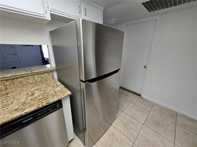 kitchen with light tile patterned floors, light stone countertops, a textured ceiling, appliances with stainless steel finishes, and white cabinetry