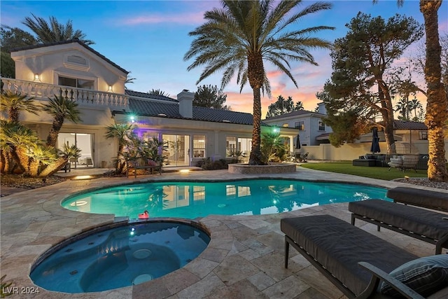 pool at dusk featuring an in ground hot tub and a patio