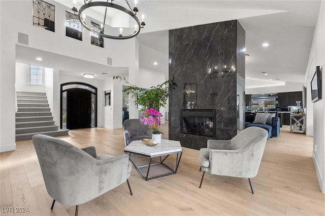 living room featuring a fireplace, light hardwood / wood-style floors, a chandelier, and a high ceiling