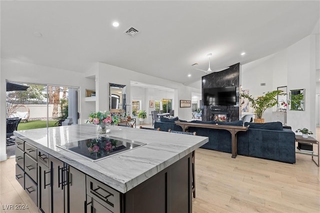 kitchen featuring light hardwood / wood-style flooring, light stone counters, black electric stovetop, a large fireplace, and a kitchen island