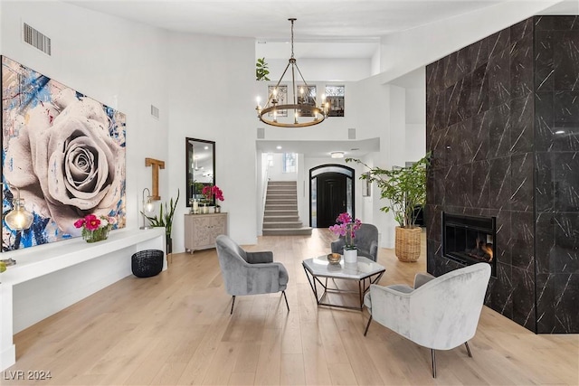 living area with hardwood / wood-style flooring, a large fireplace, an inviting chandelier, and a high ceiling