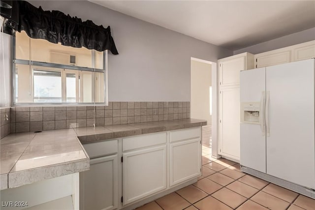 kitchen featuring tile countertops, white cabinetry, white fridge with ice dispenser, and light tile patterned floors