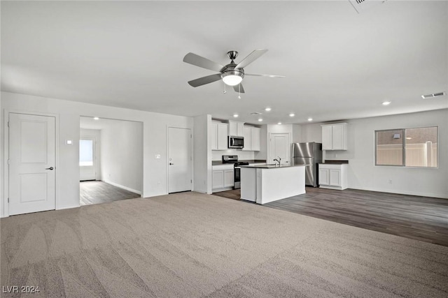 unfurnished living room featuring dark colored carpet, ceiling fan, and sink