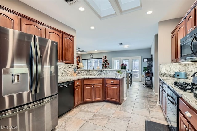 kitchen with light stone countertops, sink, tasteful backsplash, kitchen peninsula, and black appliances