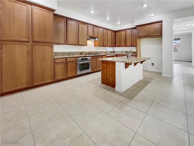 kitchen featuring appliances with stainless steel finishes, light stone counters, a breakfast bar, a kitchen island with sink, and sink