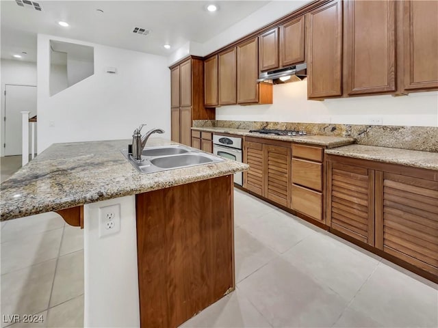 kitchen with a center island with sink, light stone countertops, sink, and appliances with stainless steel finishes