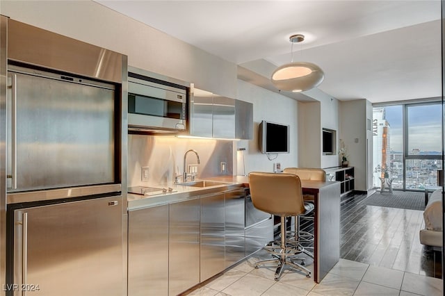 kitchen with pendant lighting, sink, built in appliances, stainless steel counters, and a wall of windows