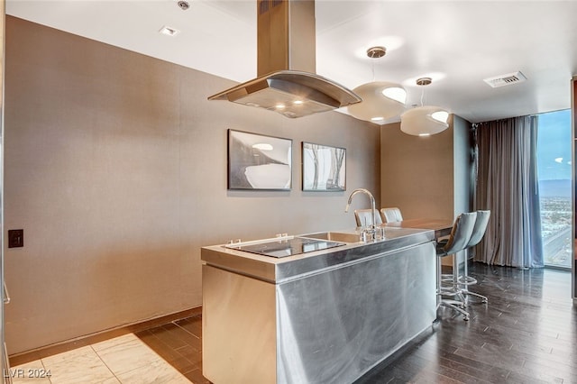 kitchen featuring sink, dark hardwood / wood-style floors, island exhaust hood, electric cooktop, and a breakfast bar