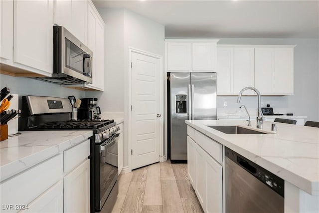 kitchen with light stone counters, stainless steel appliances, light hardwood / wood-style floors, white cabinets, and sink