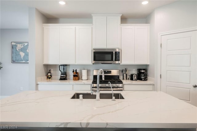 kitchen featuring light stone countertops, an island with sink, white cabinetry, appliances with stainless steel finishes, and sink