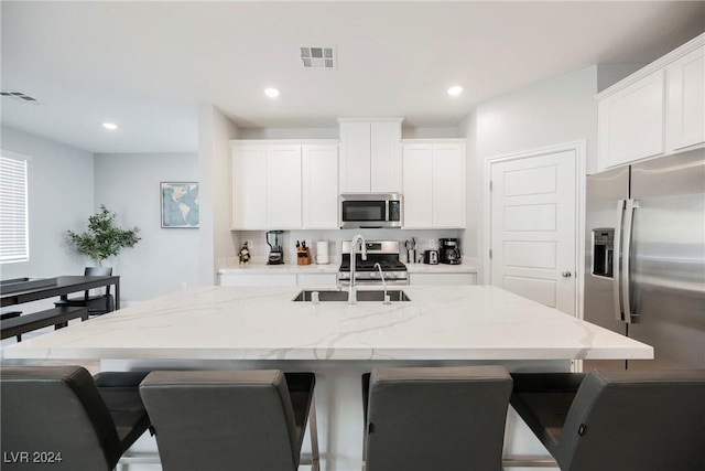 kitchen featuring stainless steel appliances, a kitchen island with sink, white cabinets, and a breakfast bar area