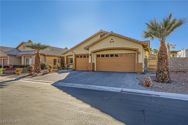 mediterranean / spanish house featuring an attached garage, fence, a tile roof, decorative driveway, and stucco siding