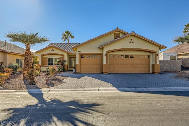 mediterranean / spanish-style house featuring decorative driveway, an attached garage, fence, and stucco siding