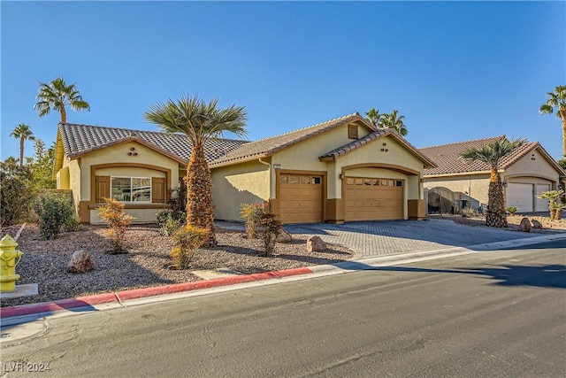 mediterranean / spanish home with a garage, decorative driveway, a tile roof, and stucco siding