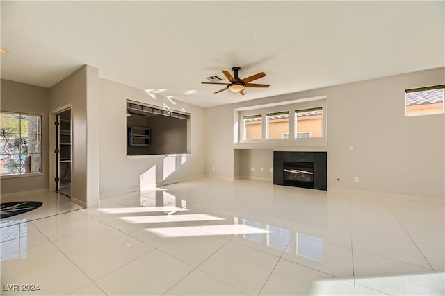 unfurnished living room with ceiling fan, light tile patterned floors, a tile fireplace, and a wealth of natural light