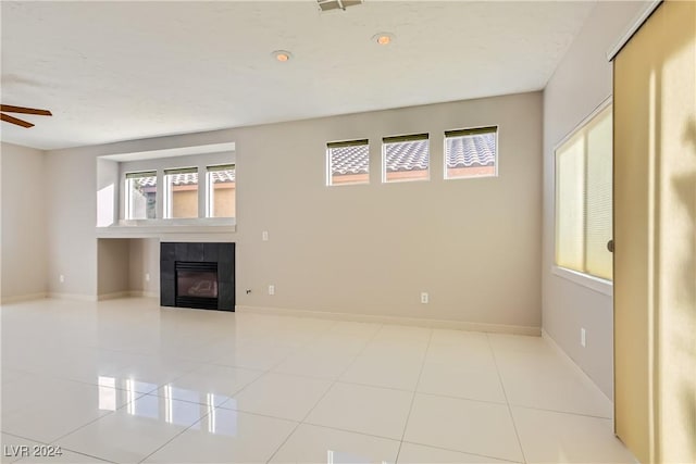 unfurnished living room featuring ceiling fan, plenty of natural light, a tile fireplace, and light tile patterned floors