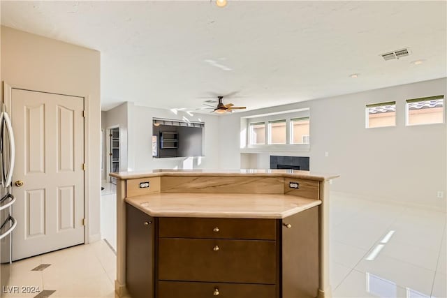 kitchen with ceiling fan, light tile patterned flooring, dark brown cabinetry, and a tiled fireplace