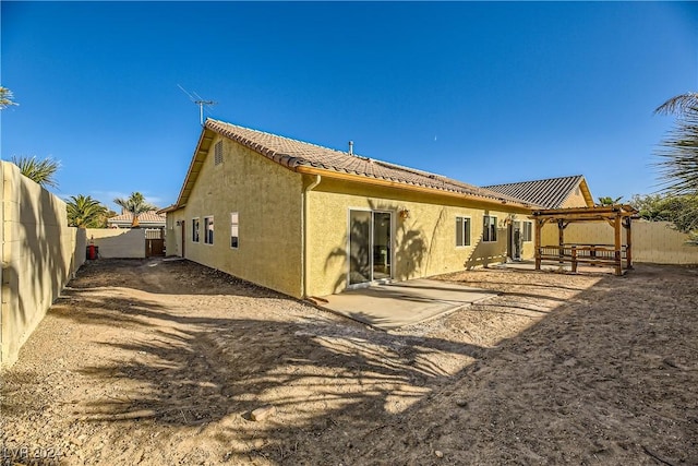 rear view of house with stucco siding, a tile roof, a fenced backyard, and a patio