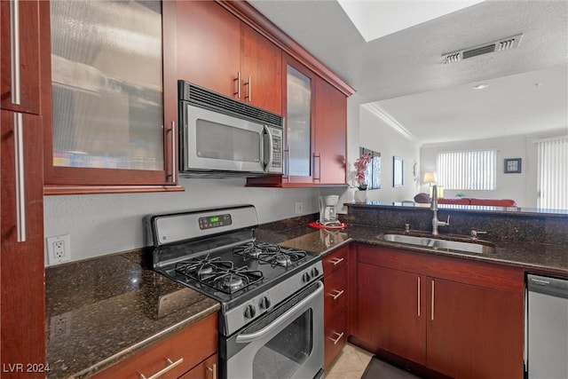 kitchen with appliances with stainless steel finishes, dark stone counters, a textured ceiling, sink, and light tile patterned flooring