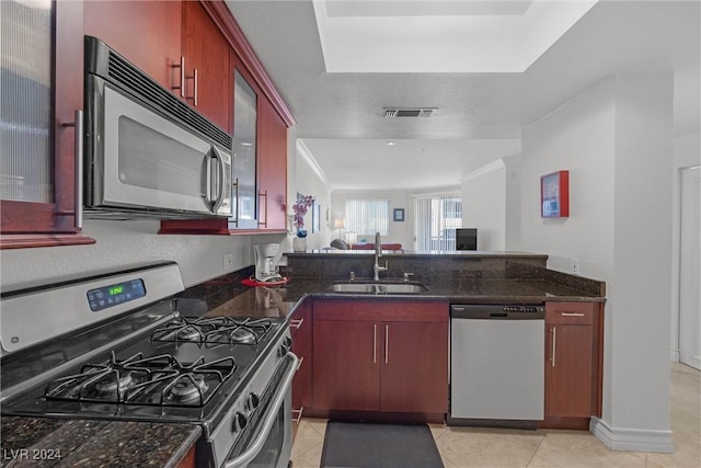 kitchen with sink, stainless steel appliances, dark stone countertops, a textured ceiling, and light tile patterned floors