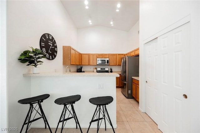 kitchen featuring high vaulted ceiling, light tile patterned floors, a kitchen bar, kitchen peninsula, and stainless steel appliances