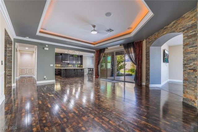 unfurnished living room with dark wood-type flooring, a tray ceiling, and crown molding