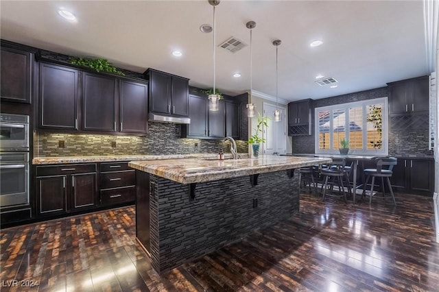 kitchen with pendant lighting, a kitchen breakfast bar, dark hardwood / wood-style floors, and an island with sink