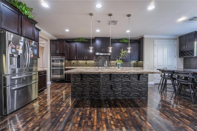 kitchen with a kitchen bar, an island with sink, pendant lighting, and appliances with stainless steel finishes