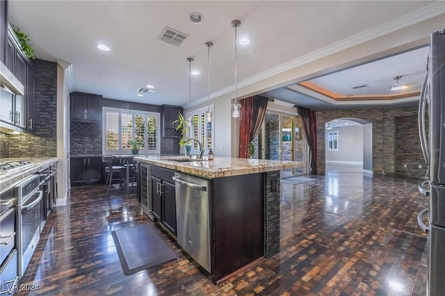 kitchen with backsplash, a kitchen island with sink, crown molding, decorative light fixtures, and stainless steel appliances