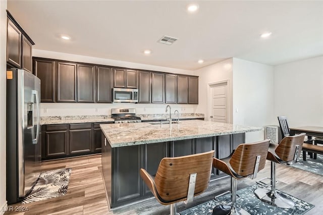 kitchen with light wood-type flooring, stainless steel appliances, a kitchen island with sink, and sink