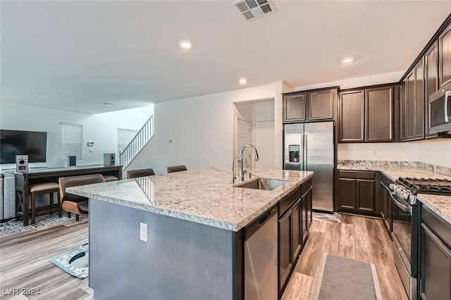 kitchen with a kitchen breakfast bar, sink, an island with sink, light hardwood / wood-style floors, and stainless steel appliances