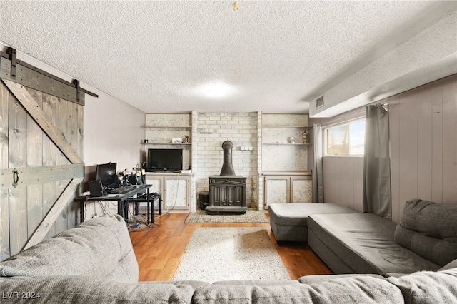 living room featuring a textured ceiling, a barn door, hardwood / wood-style floors, a wood stove, and wood walls