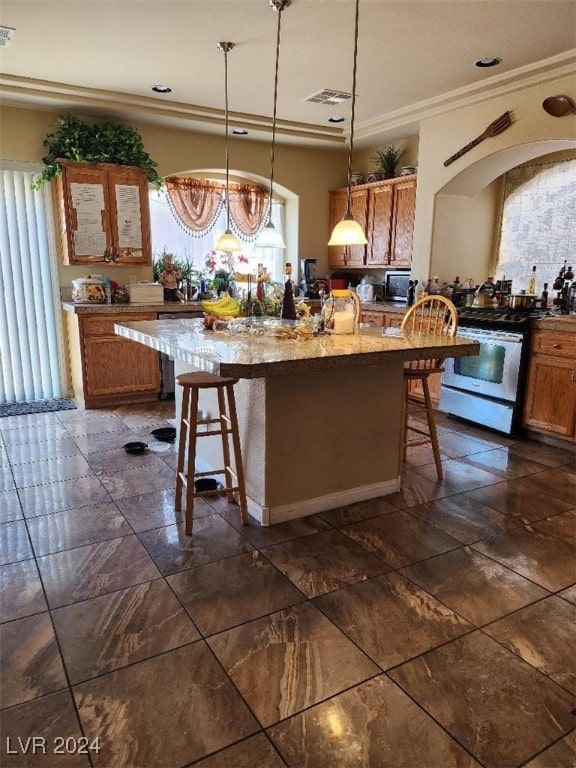 kitchen featuring white gas range, crown molding, decorative light fixtures, a kitchen island with sink, and a breakfast bar